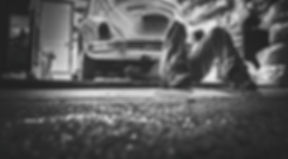 Technician working underneath a vehicle in a low-lit garage
